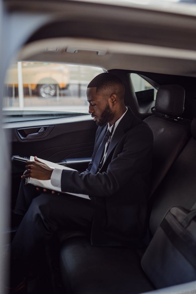 A business professional in a suit reading documents inside a car.