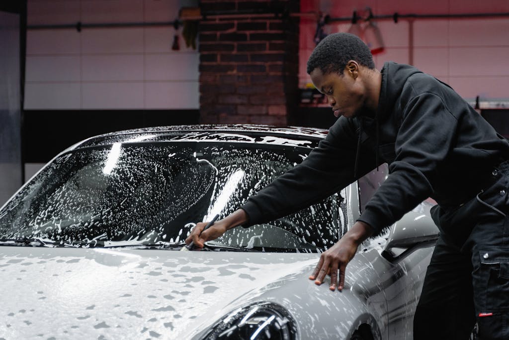 A man cleans a luxury sports car with soap in an indoor garage setting.