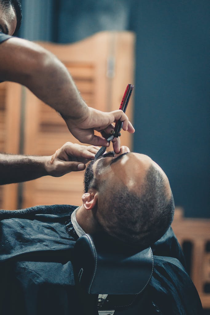 Close-up of a barber expertly shaving a man's beard indoors, showcasing precision and care.