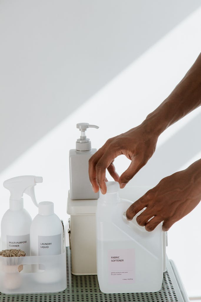 Close-up of hands organizing various cleaning products on a white surface, showcasing cleanliness and home care essentials.